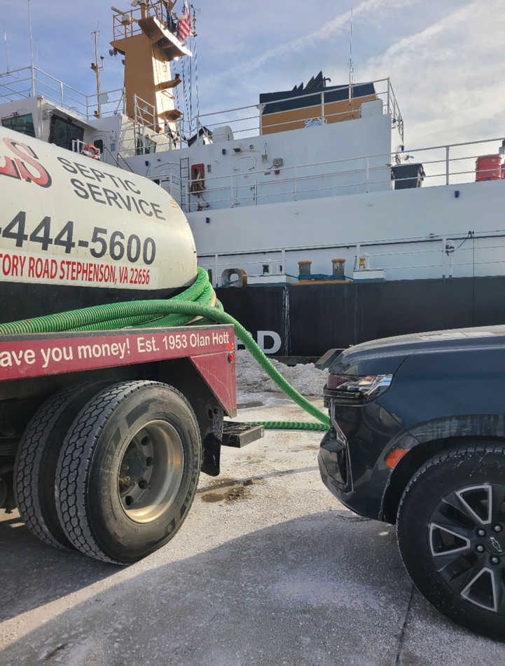 Back end of Septic truck connected to hose. Truck is in front of a large boat